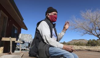 Raymond Clark sits outside his home in Teesto, Ariz., on the Navajo Nation on Thursday, Feb. 11, 2021. Teesto workers, health representatives, volunteers and neighbors keep close tabs on another to ensure the most vulnerable citizens get the help they need. (AP Photo/Felicia Fonseca)