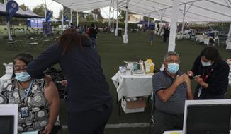 Healthcare workers inject people with the Sinovac COVID-19 vaccine at La Pintana Sports Complex turned into a makeshift vaccination site, in Santiago, Chile, Thursday, March 11, 2021, on the one-year anniversary that the World Health Organization declared the coronavirus a pandemic. (AP Photo/Esteban Felix)