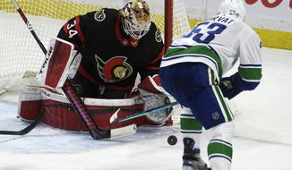 Vancouver Canucks center Bo Horvat tries to control the puck in front of Ottawa Senators&#39; goaltender Joey Daccord during the second period of an NHL hockey game in Ottawa, Ontario, Monday, March 15, 2021. (Adrian Wyld/The Canadian Press via AP)