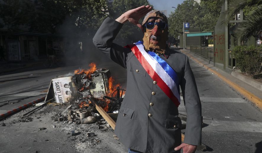 FILE - In this Nov. 6, 2019 file photo, an anti-government demonstrator costumed as late military dictator Gen. Augusto Pinochet salutes in front of a burning street barricade placed by protesters demanding a new constitution in Santiago, Chile. Chileans will elect an assembly on April 11, 2021, tasked with writing fresh governing principles and putting them to a national vote in the first half of 2022 to replace the much-amended relic of military rule, the 1980 constitution. (AP Photo/Esteban Felix, File)