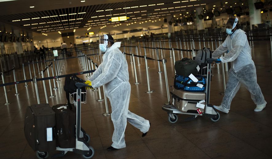 FILE - In this July 29, 2020 file photo, passengers wearing full protective gear against the spread of coronavirus, push their luggage in the departure hall of Zaventem international airport in Brussels. As curfew-weary, mask-wearing European citizens hope for relief, and perhaps the prospect of a real summer vacation this year, at an upcoming EU summit on Thursday, Feb. 25, 2021 leaders will also focus on when to ease restrictions, and the possibility of a future vaccination certificate so people can travel more conveniently. (AP Photo/Francisco Seco, File)