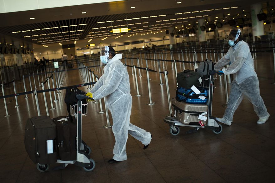 FILE - In this July 29, 2020 file photo, passengers wearing full protective gear against the spread of coronavirus, push their luggage in the departure hall of Zaventem international airport in Brussels. As curfew-weary, mask-wearing European citizens hope for relief, and perhaps the prospect of a real summer vacation this year, at an upcoming EU summit on Thursday, Feb. 25, 2021 leaders will also focus on when to ease restrictions, and the possibility of a future vaccination certificate so people can travel more conveniently. (AP Photo/Francisco Seco, File)