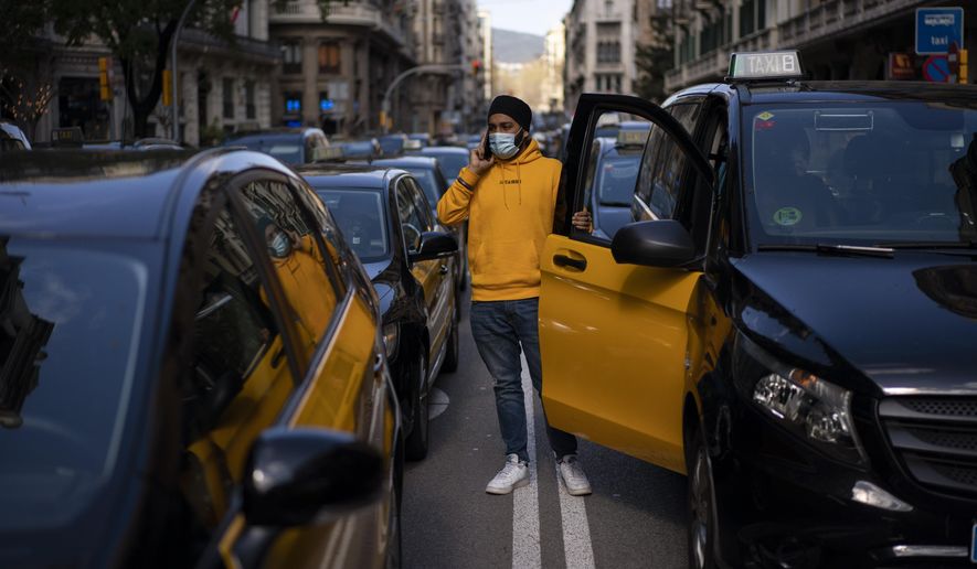 A taxi driver stands next to his cab as they march slowly blocking the traffic along one of the avenues in Barcelona downtown, Spain, Thursday, March 18, 2021. Hundreds of yellow-and-black cabs disrupted Barcelona&#39;s road traffic on Thursday to protest against the return of the ride-hailing giant Uber to the northeastern city after a 2-year hiatus. (AP Photo/Emilio Morenatti)