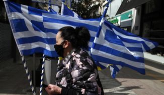 A woman wearing a face mask against the spread of coronavirus, walks in front of Greek flags which are for sale in Athens, Friday, March 19, 2021. The military parade on March 25, marking 200-years since the war that resulted in Greece&#x27;s independence from the Ottoman Empire and rebirth as a nation, will be held without spectators due to the coronavirus, and only Greek and foreigners political officials will attend it. (AP Photo/Thanassis Stavrakis)