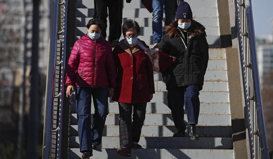 People wearing face masks to help curb the spread of the coronavirus walk down a pedestrian overhead bridge in Beijing, Sunday, March 21, 2021. (AP Photo/Andy Wong)