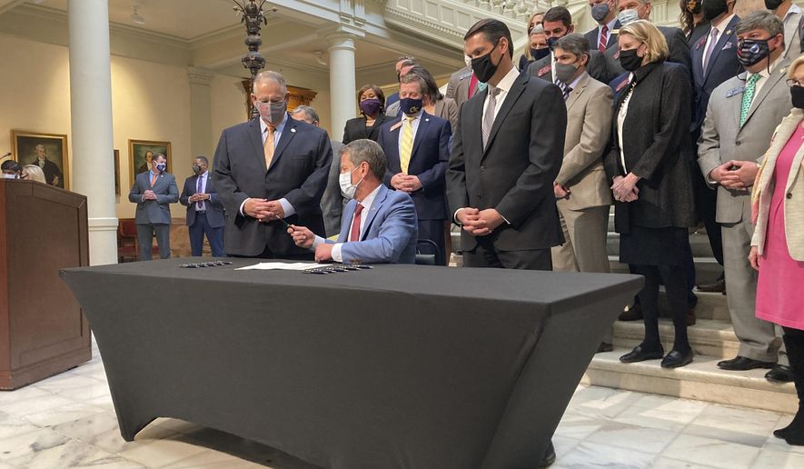 Georgia Gov. Brian Kemp, seated, hands a pen to Georgia House Speaker David Ralston on Monday, March 22, 2021, at the state capitol in Atlanta after signing a tax cut bill. The measure would raise the amount of money someone can earn before paying state income taxes, saving most individual filers up to $43. (AP Photo/Jeff Amy)