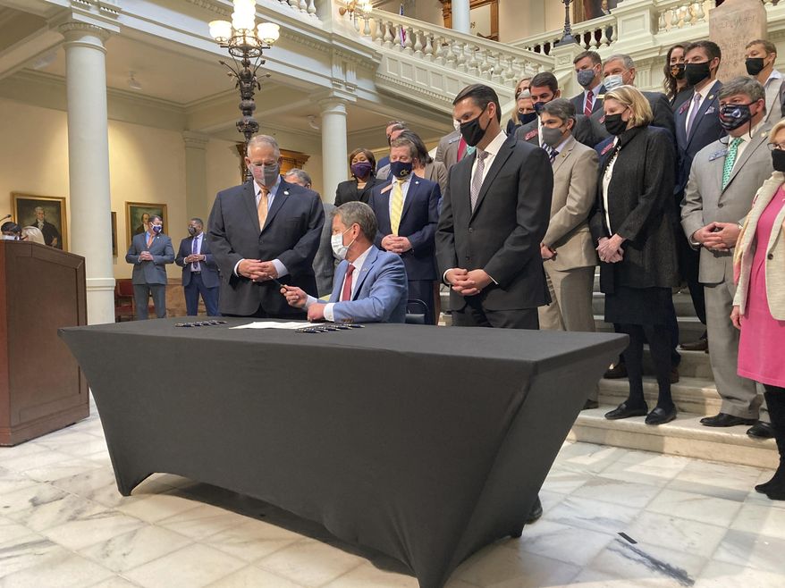 Georgia Gov. Brian Kemp, seated, hands a pen to Georgia House Speaker David Ralston on Monday, March 22, 2021, at the state capitol in Atlanta after signing a tax cut bill. The measure would raise the amount of money someone can earn before paying state income taxes, saving most individual filers up to $43. (AP Photo/Jeff Amy)