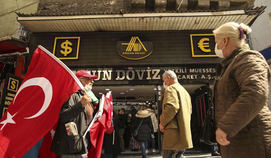 A vendor offering Turkish flags for sale walks past a currency exchange shop, at an open market Istanbul, Monday, March 22, 2021. The Turkish currency plummeted against the U.S. dollar on Monday after President Recep Tayyip Erdogan fired the central bank governor over the weekend for hiking interest rates. The lira was trading at around 7.9 against the dollar — nearly 10% down from Friday&#39;s close. Erdogan, who advocates keeping interest rates low to tame inflation, unexpectedly fired Naci Agbal with a decree on Saturday, just four months after he took office. (AP Photo/Emrah Gurel)