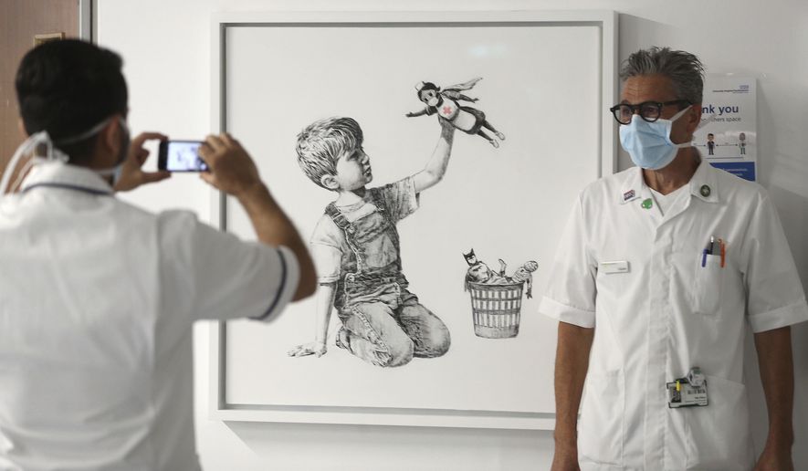 FILE - In this May 7, 2020 file photo, a member of staff has their photograph taken in front of the artwork painted by Banksy during lockdown, entitled &#39;Game Changer&#39;, at Southampton General Hospital in Southampton, England. A Banksy painting honoring Britain’s health workers in the coronavirus pandemic has sold for a record 16.8 million pounds ($23.2 million.) Auction house Christie’s said Tuesday, March 23, 2021 that proceeds from the sale will be used to fund health organizations and charities across the U.K. (Andrew Matthews/PA via AP, file)