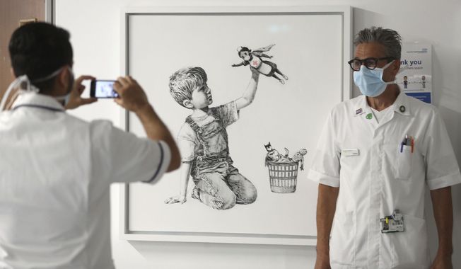 FILE - In this May 7, 2020 file photo, a member of staff has their photograph taken in front of the artwork painted by Banksy during lockdown, entitled &#x27;Game Changer&#x27;, at Southampton General Hospital in Southampton, England. A Banksy painting honoring Britain’s health workers in the coronavirus pandemic has sold for a record 16.8 million pounds ($23.2 million.) Auction house Christie’s said Tuesday, March 23, 2021 that proceeds from the sale will be used to fund health organizations and charities across the U.K. (Andrew Matthews/PA via AP, file)