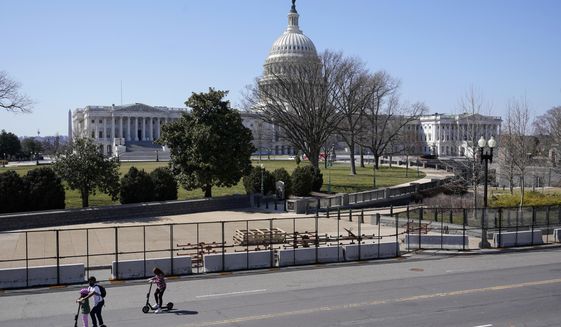 People ride scooters past an inner perimeter of security fencing on Capitol Hill in Washington, Sunday, March 21, 2021, after portions of an outer perimeter of fencing were removed overnight to allow public access. (AP Photo/Patrick Semansky)