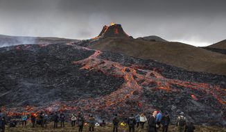 People watch and take photos as lava flows from an eruption of a volcano on the Reykjanes Peninsula in southwestern Iceland on Tuesday, March 23, 2021. Iceland&#39;s latest volcano eruption is quickly attracting crowds of people hoping to get close to the gentle lava flows. The eruption in Geldingadalur, near Iceland&#39;s capital Reykjavik, is not seen as a threat to nearby towns and the slow flows mean people can get close to action without too much harm. (AP Photo/Marco Di Marco)