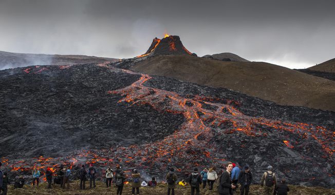 People watch and take photos as lava flows from an eruption of a volcano on the Reykjanes Peninsula in southwestern Iceland on Tuesday, March 23, 2021. Iceland&#x27;s latest volcano eruption is quickly attracting crowds of people hoping to get close to the gentle lava flows. The eruption in Geldingadalur, near Iceland&#x27;s capital Reykjavik, is not seen as a threat to nearby towns and the slow flows mean people can get close to action without too much harm. (AP Photo/Marco Di Marco)