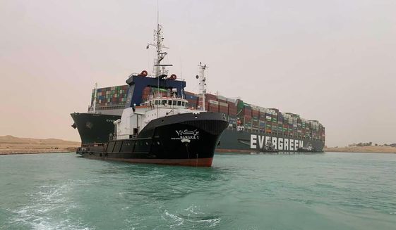 In this photo released by the Suez Canal Authority, a boat navigates in front of a cargo ship, Ever Given, Wednesday, March 24, 2021, after it becomes wedged across Egypt’s Suez Canal and blocked all traffic in the vital waterway. An Egyptian official warned Wednesday it could take at least two days to clear the ship. (Suez Canal Authority via AP)