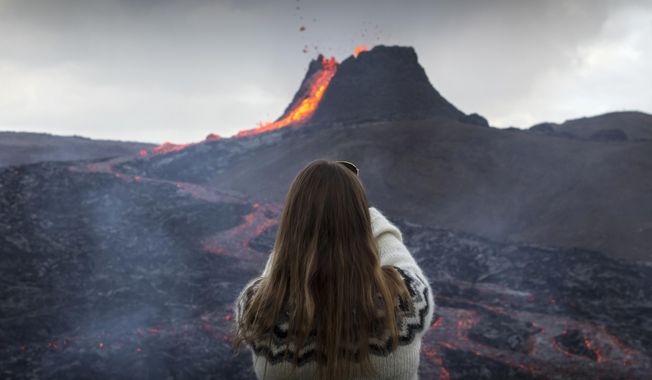 A woman takes a photo as lava flows from an eruption of a volcano on the Reykjanes Peninsula in southwestern Iceland on Tuesday, March 23, 2021. Iceland&#x27;s latest volcano eruption is quickly attracting crowds of people hoping to get close to the gentle lava flows. The eruption in Geldingadalur, near Iceland&#x27;s capital Reykjavik, is not seen as a threat to nearby towns and the slow flows mean people can get close to action without too much harm. (AP Photo/Marco Di Marco)