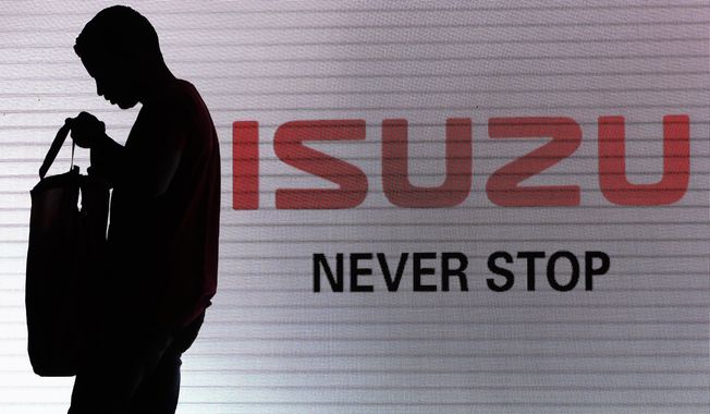 FILE - In this May 11, 2017, file photo, a man walks past the Isuzu logo during the launch of Isuzu MU-X SUV in New Delhi, India. Japanese automakers Toyota, Isuzu and Hino said Wednesday, March 24, 2021 they are setting up a partnership in commercial vehicles to work together in electric, hydrogen, connected and autonomous driving technologies. (AP Photo/Tsering Topgyal, File)