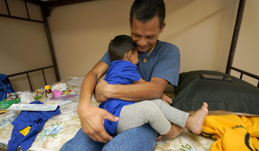 Elmer Maldonado, top, a migrant from Honduras, hugs his 1-year-old son at a shelter, Monday, March 22, 2021, in Harlingen, Texas. They spent a week in immigration custody after crossing the Rio Grande through Texas to request asylum. His experience illustrates a cycle that is repeating itself thousands of times a week amid a dramatic rise in migrant children and families at the U.S.-Mexico border: They arrive in the middle of the night by the dozens and are kept at outdoor intake sites, then taken to overcrowded detention facilities well past the 72-hour court-imposed limit. (AP Photo/Julio Cortez)