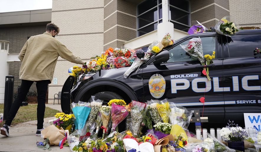 In this March 23, 2021, photo, a man leaves a bouquet on a police cruiser parked outside the Boulder Police Department after an officer was one of the victims of a mass shooting at a King Soopers grocery store in Boulder, Colo. The suspects in the most recent shooting sprees found it relatively easy to get their guns. The suspect in the shooting at a Boulder supermarket was convicted of assaulting a high school classmate but still got a gun.(AP Photo/David Zalubowski)