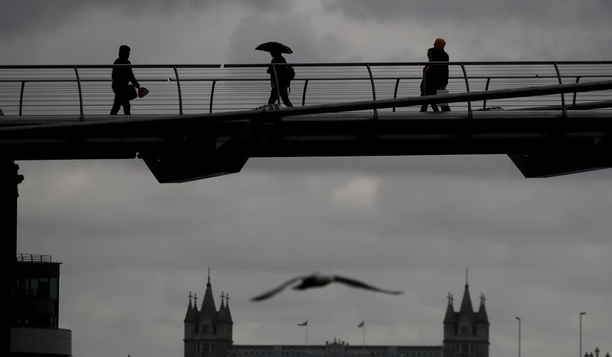 People are silhouetted as they walk over Millennium Bridge during rainy weather, as the coronavirus lockdown continues in London, Thursday, March 25, 2021. (AP Photo/Kirsty Wigglesworth)