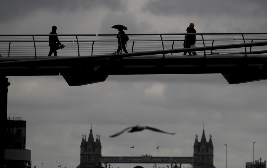 People are silhouetted as they walk over Millennium Bridge during rainy weather, as the coronavirus lockdown continues in London, Thursday, March 25, 2021. (AP Photo/Kirsty Wigglesworth)