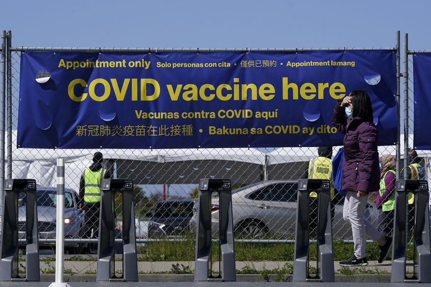 A pedestrian wears a face mask while walking past a sign at a vaccination center at City College of San Francisco during the coronavirus pandemic in San Francisco, Thursday, March 25, 2021. (AP Photo/Jeff Chiu) ** FILE **