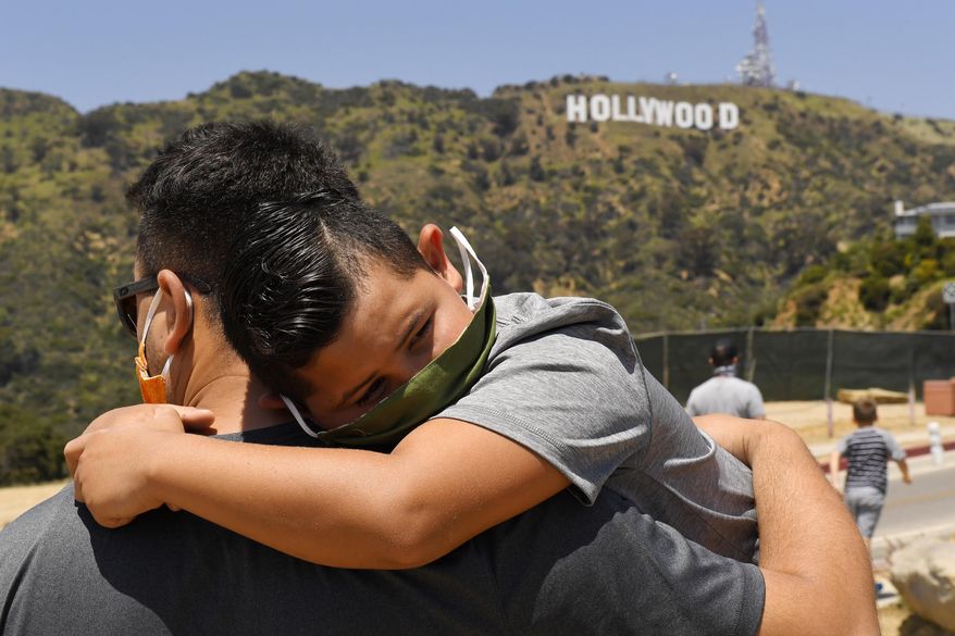 FILE - In this May 15, 2020, file photo, a father holds his son near the famed Hollywood sign during the coronavirus outbreak in Los Angeles. (AP Photo/Mark J. Terrill, File)
