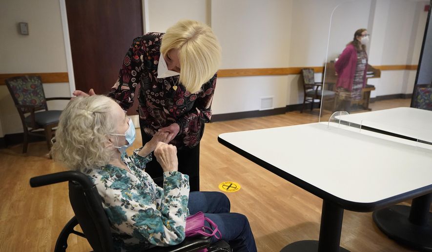 FILE - In this March 18, 2021, file photo, Mary Claire Lane, 86, left, a resident at Hellenic Nursing and Rehabilitation Center, in Canton, Mass., is greeted by her daughter Anne Darling, of Attleboro, Mass., center, during a visit,  at the nursing home, in Canton. Nursing homes have to publicly disclose their vaccination rates for flu and pneumonia, but there’s no similar mandate for COVID-19 shots. (AP Photo/Steven Senne, File)