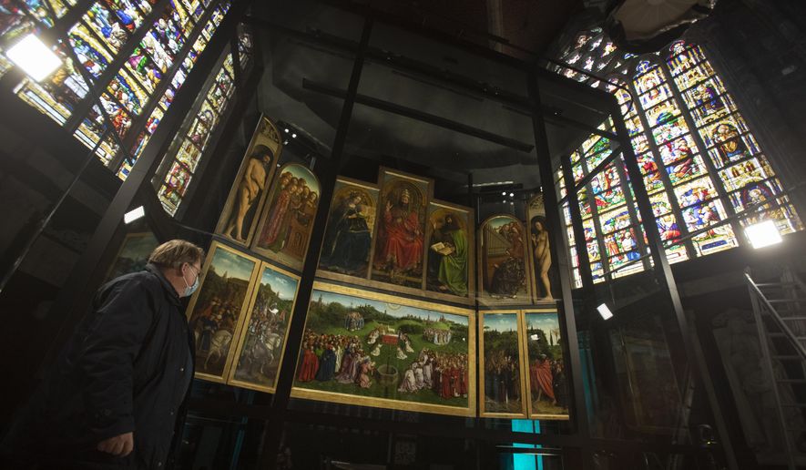 A man views the panels of the Ghent Altarpiece, by Flemish painter Jan Van Eyck, at Saint Bavo Cathedral in Ghent, Belgium on Monday, March 22, 2021. The Saint Bavo Cathedral will open a new visitors center where the restored Ghent Altarpiece will be the focal point. The 1934 theft of one of the panels, the Just Judges, and the restoration of the work, are testament to perhaps one of the greatest unsolved art crimes of all time. (AP Photo/Virginia Mayo)