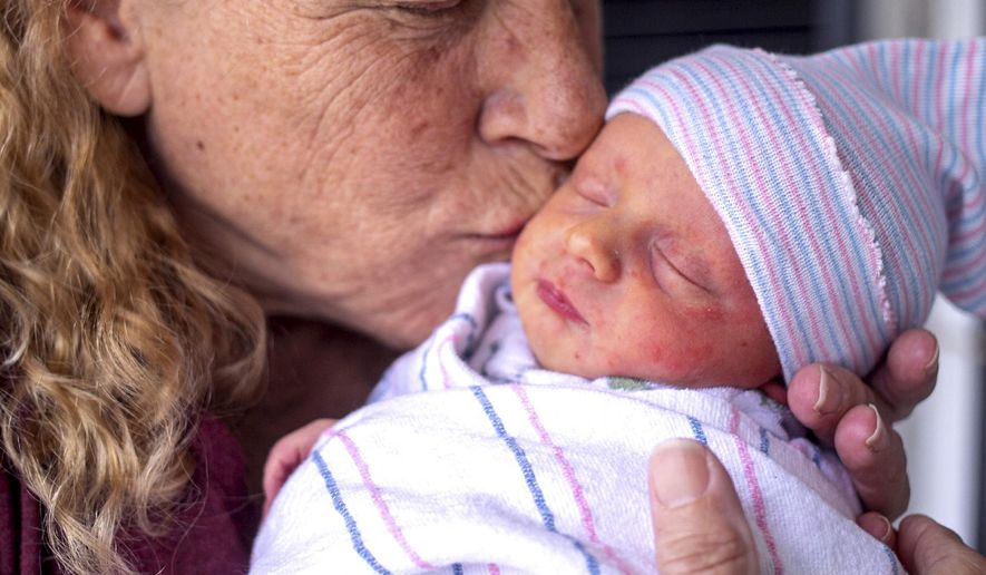 Barbara Higgins cradles her newborn's head in her the family home on Wednesday, March 24, 2021 in Concord, N.H. Higgins who lost her 13-year-old daughter to a brain tumor in 2016 has given birth to a son at age 57. Barbara Higgins, and her husband, Kenny Banzhoff, of Concord, have been dealing with grief over the death of their daughter, Molly. (Geoff Forester/The Concord Monitor via AP)