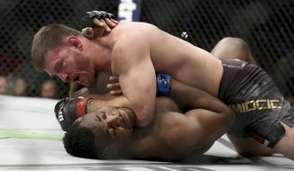 FILE - Stipe Miocic, top, presses his elbow into the throat of Francis Ngannou during a heavyweight championship mixed martial arts bout at UFC 220 in Boston, in this early Sunday, Jan. 21, 2018, file photo. Stipe Miocic hasn’t fought anybody except Daniel Cormier in three years, and the UFC’s heavyweight champion is ready for a new challenge. Instead, he’s getting a rematch at UFC 260 with dangerous Francis Ngannou, who believes he’s mentally ready to claim the title he couldn’t take from the modest king of the division in 2018. (AP Photo/Gregory Payan, File)