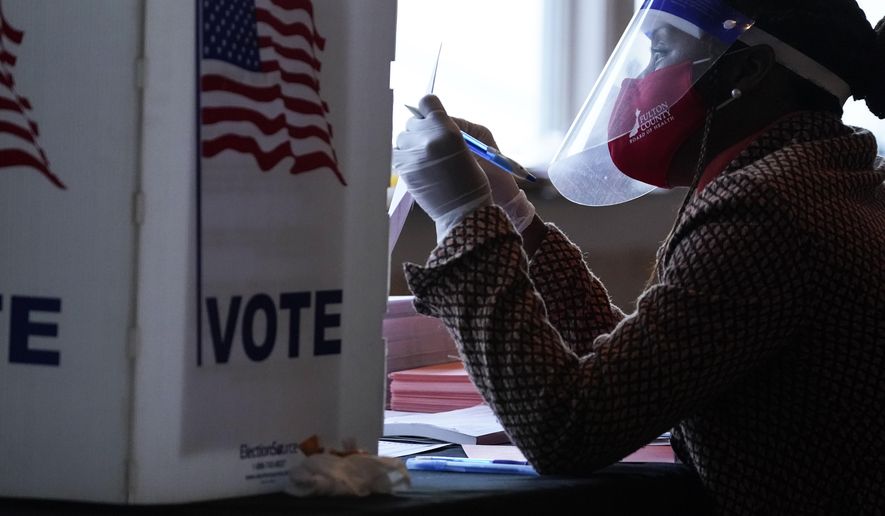 FILE - In this Nov. 3, 2020, file photo, a poll worker talks to a voter before they vote on a paper ballot on Election Day in Atlanta. In addition to their nationwide efforts to restrict voting access, Republican lawmakers in some key states are seeking greater control over the local mechanics of elections, from voter registration to certifying results. It's part of a broader GOP campaign to limit access to the ballot and challenge outcomes. (AP Photo/Brynn Anderson, File)