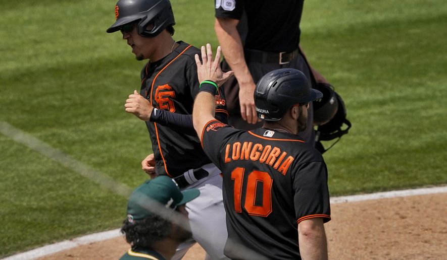 San Francisco Giants' Wilmer Flores and Evan Longoria (10) score on a double hit by Curt Casali during the third inning of a spring training baseball game against the Oakland Athletics, Monday, March 29, 2021, in Mesa, Ariz. (AP Photo/Matt York)