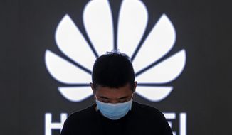 FILE - In this Aug. 31, 2020, file photo, an employee wearing a face mask to help curb the spread of the coronavirus stands inside a Huawei flagship store in Beijing.  Chinese tech giant Huawei said Wednesday, March 31, 2021, it eked out a gain in sales and profit last year but growth plunged after its smartphone unit was hammered by U.S. sanctions imposed in a fight with Beijing over technology and security.(AP Photo/Andy Wong, File)