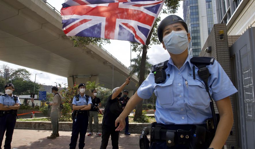 A pro-democracy supporter waves a British flag as police officers stand guard outside a court in Hong Kong Thursday, April 1, 2021. Seven pro-democracy advocates, including media tycoon Jimmy Lai and veteran of the city&#x27;s democracy movement Martin Lee, are expected to be handed a verdict for organizing and participating in an illegal assembly during massive anti-government protests in 2019 as Hong Kong continues its crackdown on dissent. (AP Photo/Vincent Yu)
