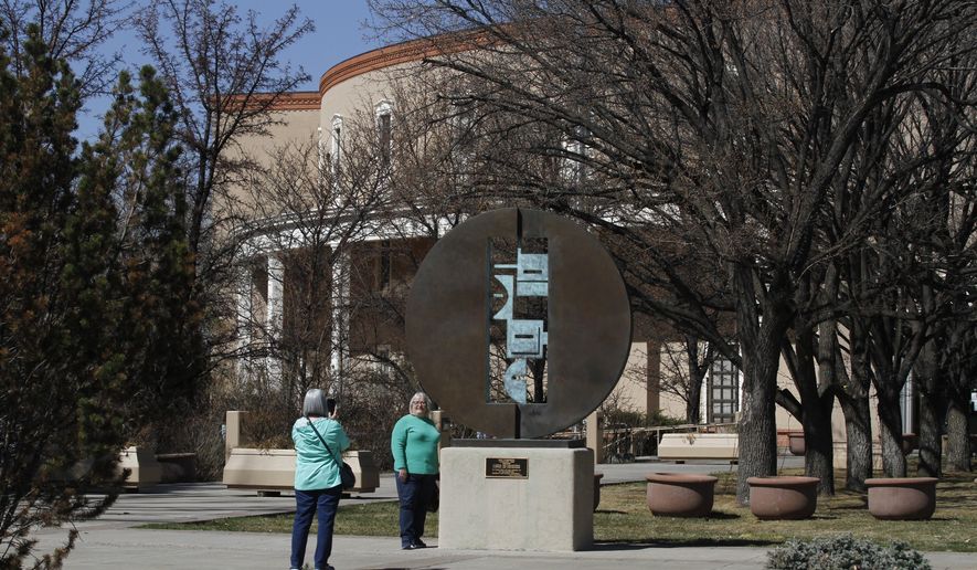 Tourist Rene Greenmyer takes a picture of her friend Dawn Plonkey, outside the state capitol building on Tuesday, March 30, 2021, in Santa Fe, New Mexico. The Arizona residents happened to pass by the 1999 bronze sculpture "Passage," by Dan Namingha as New Mexico lawmakers met in a special session to revisit a sprawling set of marijuana legalization proposals that led to a deadlock during the regular session earlier in March. Plonkey says she doesn't use marijuana but voted in favor of a ballot initiative to legalize it in Arizona. (AP Photo/Cedar Attanasio)
