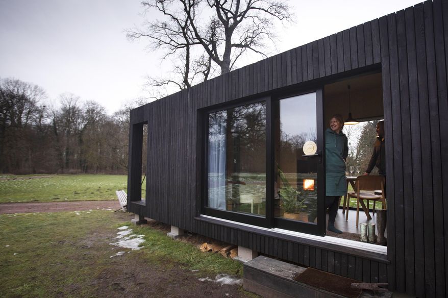 Kim Devos, from Erpe, Belgium looks out the sliding door of a Slow Cabin in Elewijt, Belgium, Monday, Feb. 15, 2021. These Slow Cabins, set up the Belgian countryside, are the new way to vacation in pandemic times: in complete solitude and in the middle of nowhere. The wooden cabins are fully sustainable, provided you don't stay in the shower too long and you can live without Wi-Fi. (AP Photo/Virginia Mayo)
