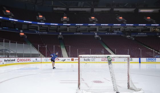 Vancouver Canucks goalie Thatcher Demko walks on the ice and shoots a puck around after the team&#39;s NHL hockey game against the Calgary Flames was postponed due to a positive COVID-19 test result in Vancouver, British Columbia, Wednesday, March 31, 2021. (Darryl Dyck/The Canadian Press via AP)