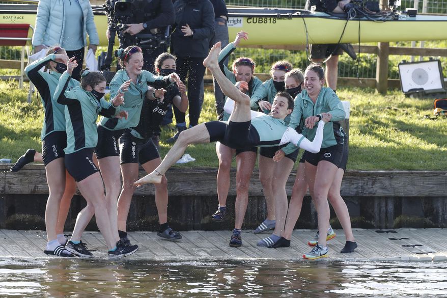 Cambridge celebrate by throwing their cox Dylan Whitaker in the river after winning the Varsity Women's Boat Race on the Great Ouse river at Ely in Cambridgeshire, England, Sunday April 4, 2021. The traditional Boat Race competition between the boat crews of Oxford and Cambridge will be staged in Ely for the first time since 1944, where the remote Fenland location will help the organizers meet the challenges of staging the event without spectators due to COVID-19 restrictions. (Paul Childs, Pool via AP)