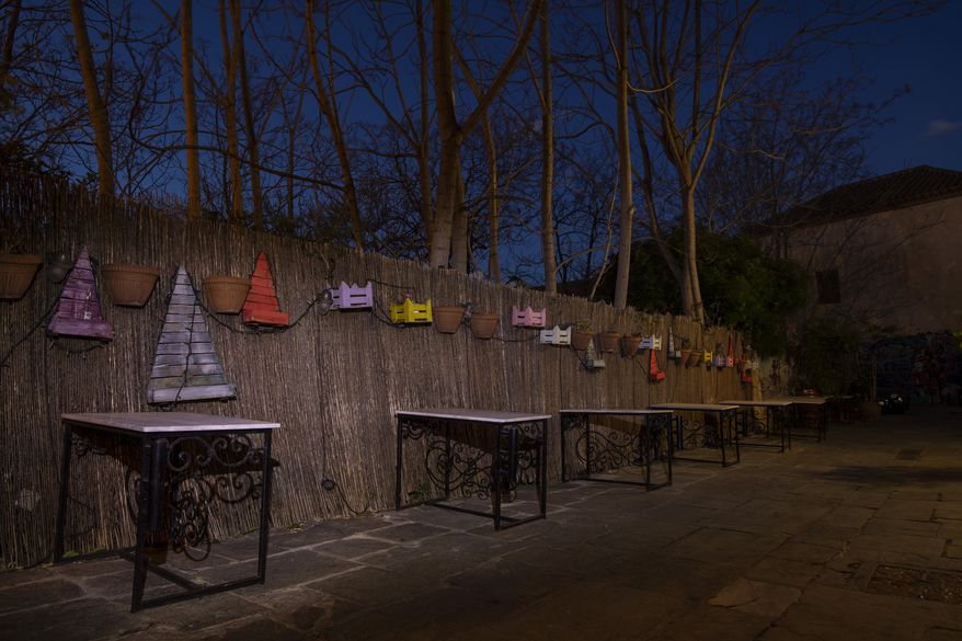 Iron tables stand in front of a decorated fence outside a shuttered traditional restaurant in Plaka, district of Athens, on Tuesday, March 16, 2021. Restaurants, bars and cafes, whose nature it is to gather groups of people closely together, have remained shut since November when the Greek government imposed a second lockdown to curb the spread of COVID-19 infections. (AP Photo/Petros Giannakouris)