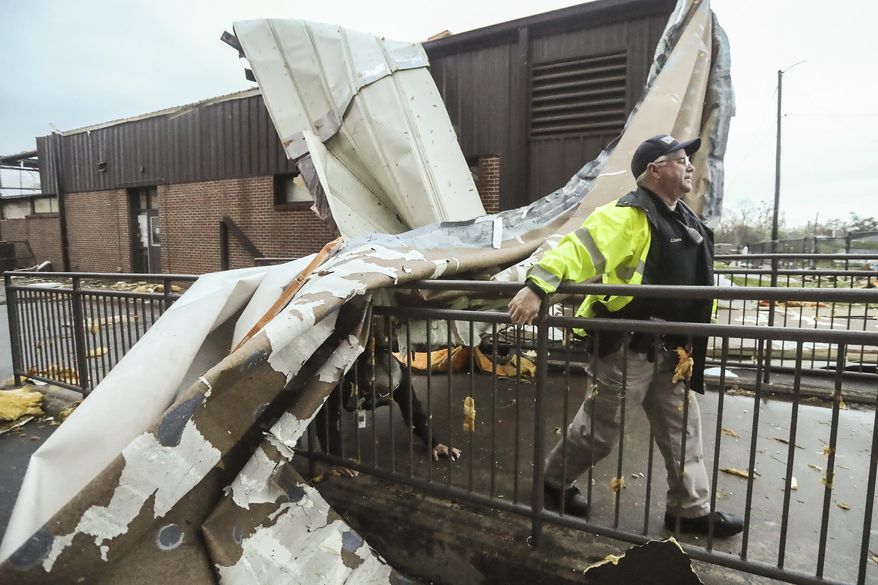 An officer moves near debris at Newnan High School, in Newnan, in Coweta County, Ga. on Friday, March 26, 2021, after a tornado moved through the area. Meteorologists say one large, dangerous tornado moved through western Georgia early Friday, downing trees and power lines. (John Spink/Atlanta Journal-Constitution via AP)