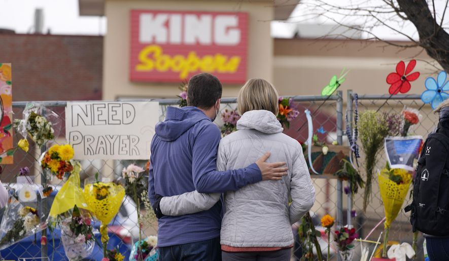 Mourners walk the temporary fence line outside the parking lot of a King Soopers grocery store, the site of a mass shooting in which 10 people died, Friday, March 26, 2021, in Boulder, Colo. (AP Photo/David Zalubowski)