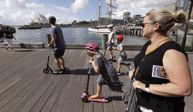 A family ride scooters as they travel along a popular boardwalk overlooking the Opera House in Sydney, Australia, Tuesday, April 6, 2021. New Zealand announced a long-anticipated travel bubble between Australia and New Zealand that will allow people to travel between the two countries without going through quarantine, allowing families to reunite and giving a big boost to the struggling tourism industry will begin April 19. (AP Photo/Rick Rycroft)