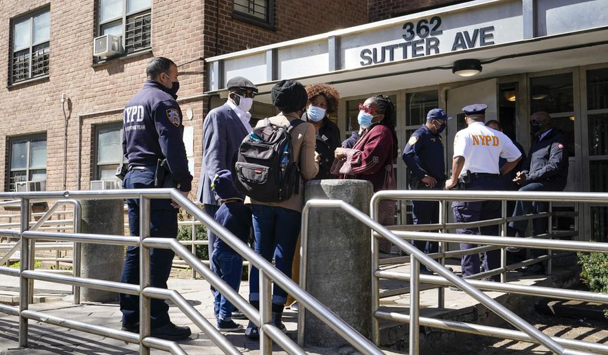 Police officers and community leaders stand outside the building where a man shot the mother of his child and two of her daughters dead before turning the gun on himself, Tuesday, April 6, 2021, in the Brownsville neighborhood of the Brooklyn borough of New York. (AP Photo/Mary Altaffer)
