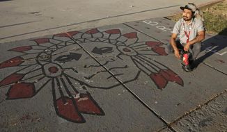 FILE - In this July 28, 2020, file photo, Native American advocate Carl Moore sits next to Native American imagery painted along a walkway which leads from the Bountiful High School parking lot up to the football field in Bountiful, Utah. A primarily white high school near Salt Lake City began replacing its hotly-contested Braves mascot after nearly 70 years. Principal Aaron Hogge announced on Friday, April 9, 2021, that the Redhawks would become Bountiful High School&#39;s mascot starting next fall. The school&#39;s new logo will be released sometime between now and the new school year. (AP Photo/Rick Bowmer, File)
