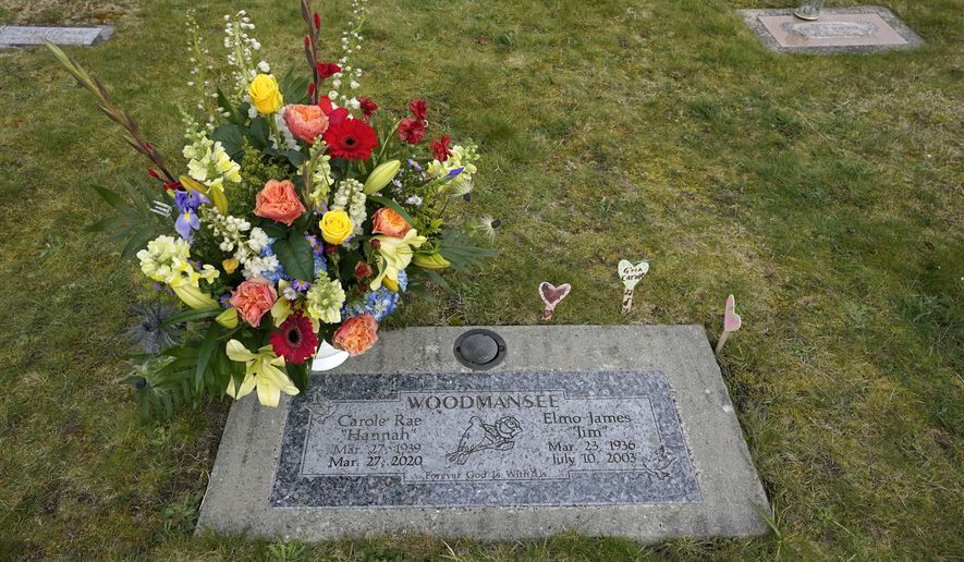 Flowers from her memorial service mark the headstone shared by Carole Rae Woodmansee and her husband Jim (who died in 2003), Saturday, March 27, 2021, at Union Cemetery in Sedro-Woolley, Wash., north of Seattle. Carole died a year ago on the same date in 2020 — the day of her 81st birthday — from complications of COVID-19 after contracting it during a choir practice that sickened 53 people and killed two — a superspreader event that would become one of the most pivotal transmission episodes in understanding the virus. (AP Photo/Ted S. Warren)