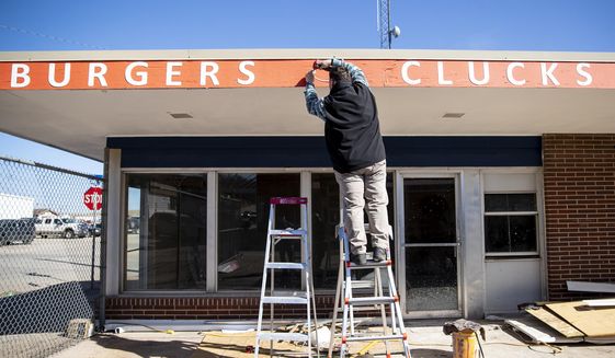Aaron Cannon attaches signage to his new business, Ranch and Roost, a burger and fried chicken restaurant, Thursday, April 1, 2021, in downtown Gillette, Wyo. Cannon and his family were among a growing number of people real estate agents say are moving to Wyoming from elsewhere. (Mike Moore/Gillette News Record via AP)