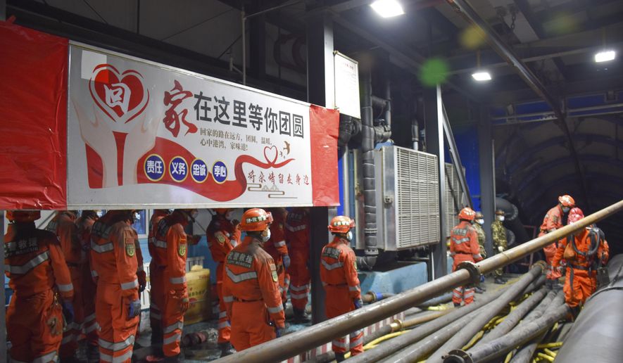 In this photo released by Xinhua News Agency, rescue workers stand near a banner which reads: "Home is waiting for your region" at the entrance to a flooded coal mine in Hutubi county in of Hui Autonomous Prefecture of Changji, northwest China's Xinjiang Uyghur Autonomous Region on Sunday, April 11, 2021. Some miners were reported trapped after the coal mine flooded on Saturday. (Gao Han/Xinhua via AP)