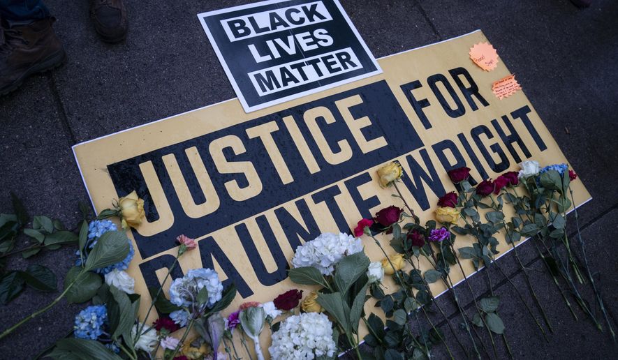 Flowers have been placed on a banner as demonstrators gather outside the Brooklyn Center (Minn.) Police Department on Tuesday, April 13, 2021, to protest Sunday&#x27;s fatal shooting of Daunte Wright during a traffic stop. (AP Photo/John Minchillo)