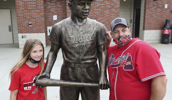 Atlanta Braves fans Pete Ciccarello and his daughter Haley pause for a photo with the statue of Jackie Robinson on Jackie Robinson Day prior to a baseball game between the Miami Marlins and Atlanta Braves in Atlanta, Thursday, April 15, 2021. (Curtis Compton/Atlanta Journal-Constitution via AP)