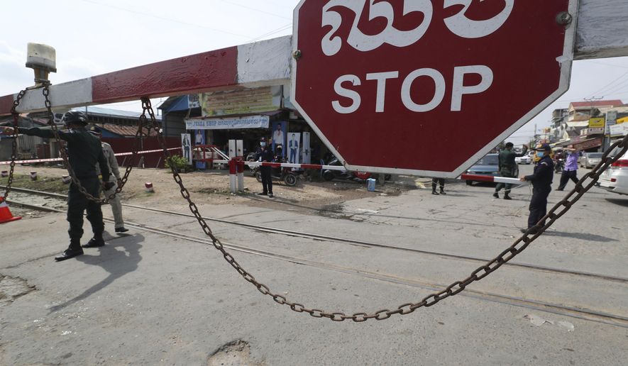 Local police officers stand guard at a blocked street near Phnom Penh International airport in Phnom Penh, Cambodia, Thursday, April 15, 2021. Cambodia’s leader said that the country’s capital Phnom Penh will be locked down for two weeks from Thursday following a sharp rise in COVID-19 cases. (AP Photo/Heng Sinith)
